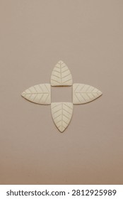 A top-down view of four cream-colored, leaf-shaped tiles with subtle vein details, arranged symmetrically in a cross formation on a solid, muted beige background. The mood is calm and aesthetic, suitable for design concepts, decor, nature themes, or craft projects