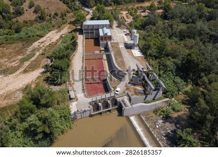 Top-down view of a gated river intake facility with potassium permanganate-dosed red water channels, concrete sedimentation basins, storage silos and processing buildings surrounded by trees