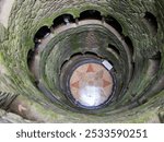 A top-down view of the Initiation Well at Quinta da Regaleira, Sintra, Portugal, with moss-covered walls and a tiled floor