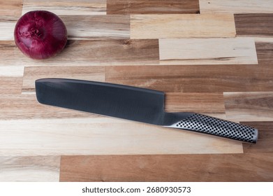 Top-down view of a kitchen knife with red onion placed on a striped wooden cutting board. Clean food preparation background for recipes, cooking, and healthy eating concepts.