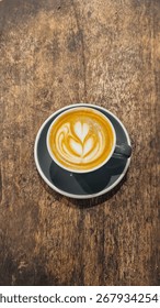 Top-down view of a latte in a ceramic cup with delicate rosette latte art, served on a rustic wooden table.