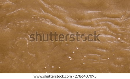 A top-down view of murky brown river water flowing with ripples and foam patterns.