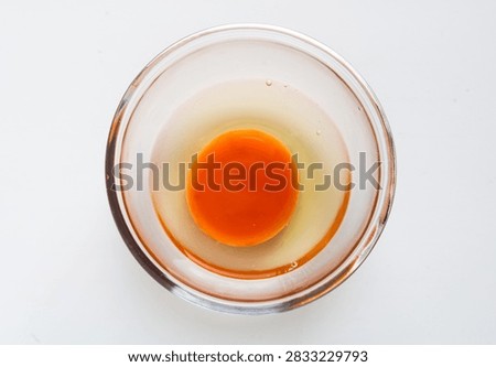 Top-down view of one raw egg inside a small round glass bowl on a white surface.