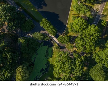 A top-down view over an empty park with a footbridge crossing a stream, surrounded by greenery.