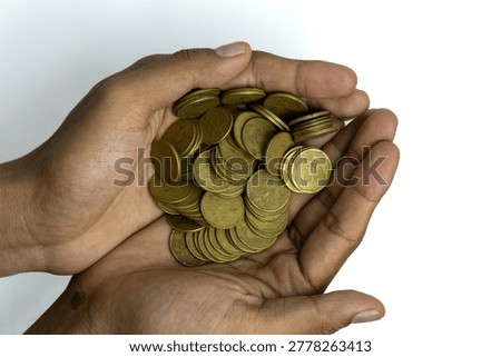 A top-down view of a pair of hands cupping a large pile of Indonesian gold-colored coins. The image symbolizes savings, charity, financial success, and wealth management. The hands are positioned in the center, isolated against a clean white background, highlighting a concept of prosperity.