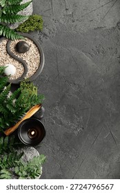 Top-down view of a peaceful zen setup with yin yang garden, candle, palo santo, moss, stones, and fern leaves on textured dark background.