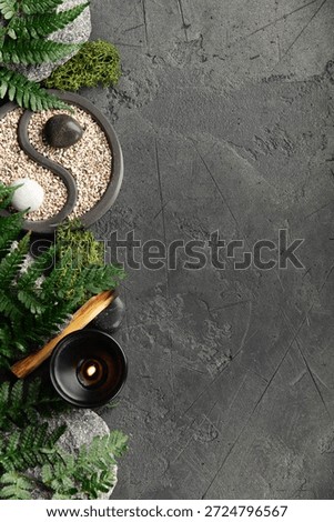Top-down view of a peaceful zen setup with yin yang garden, candle, palo santo, moss, stones, and fern leaves on textured dark background.
