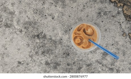 A top-down view of a plastic cup of iced coffee with a blue straw resting on a weathered concrete surface, creating a simple and refreshing minimalist composition.