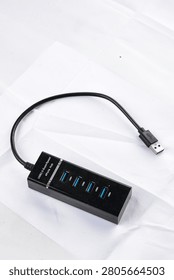top-down view of a rectangular, black 4-port USB 3.0 hub laid out on a slightly wrinkled white fabric surface