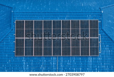 Top-down view of a rectangular photovoltaic solar array mounted on a bright blue metal roof. A concept for clean, renewable, and sustainable energy.