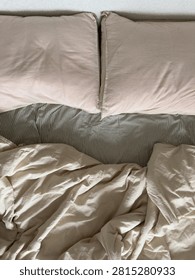 Top-down view of rumpled cream bedding and soft pink pillows with gentle folds in warm light. The unmade linens suggest a comfortable, slept-in morning.