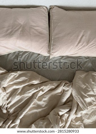 Top-down view of rumpled cream bedding and soft pink pillows with gentle folds in warm light. The unmade linens suggest a comfortable, slept-in morning.