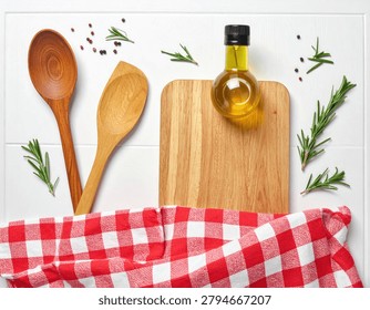 A top-down view of a rustic kitchen setting featuring wooden spoons, a cutting board, a bottle of olive oil, and fresh rosemary sprigs.