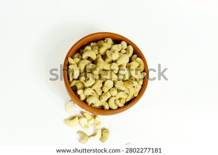 A topdown view of a rustic terracotta bowl filled with raw, organic cashew nuts, isolated on white background