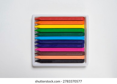 A top-down view of a set of twelve different colored wax crayons arranged neatly in a white plastic storage tray against a plain white background