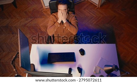 Top-down view of software engineer putting face in hands in frustration while updating binary code script on computer, receiving errors. IT worker exasperated by annoying bugs while programming.