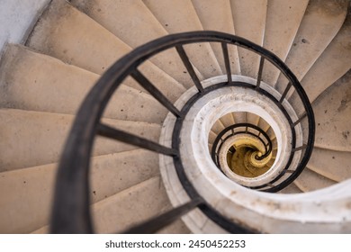 A top-down view of a spiral staircase creating an optical illusion with its descending coils. - Powered by Shutterstock