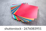 Top-down view of a stack of multicolored origami paper on a gray stone or concrete background.