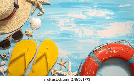 A top-down view of summer vacation items including flip-flops, sunglasses, a straw hat, seashells, and a lifebuoy on a rustic blue wooden surface.