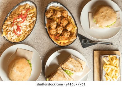 Top-down view of a table laden with diverse dishes, potatoes, burgers, chicken, sandwiches, and more. A tempting spread offering culinary variety and indulgence. High quality photo - Powered by Shutterstock