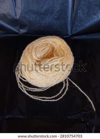 Top-down view of a thick roll of yellow wool yarn on a black background.