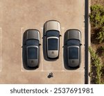 Top-down view of three cars parked in a lot, neatly aligned in individual parking spaces. The image showcases the symmetry and order of urban parking.