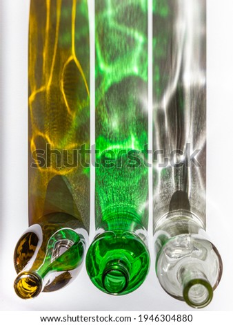 Top-down view of three empty wine bottles with creative shadows on white background. Shadows appear as colourful parallel stripes of dark orange, green, and grey with fantastic highlights.