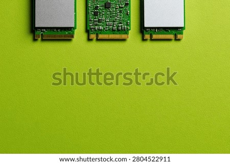 A top-down view of three M.2 NVMe Solid State Drives arranged horizontally on a bright green surface, highlighting computer hardware.