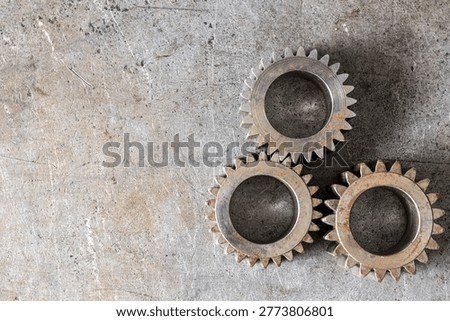 A top-down view of three metallic cogwheels placed on a weathered industrial surface with significant copy space on the left.