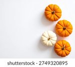 A top-down view of three small orange pumpkins and one small white pumpkin arranged on a bright white surface, creating a simple and clean autumn or Halloween themed image.