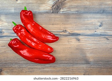Top-down view of three vibrant red peppers resting on a rustic wooden surface. 