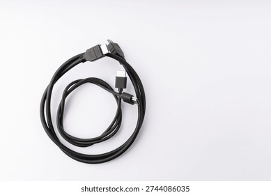 A top-down view of two indispensable black electronic cables, an HDMI cable and a USB cable, arranged in a loose, intertwined coil on a clean white background. The image clearly showcases the gold-plated HDMI connector and a silver-tipped USB connector. The bright, even studio lighting highlights the textures and shapes of the cables, making them suitable for e-commerce, tech publications, or digital communication themes. The minimalist setting provides ample copy space.