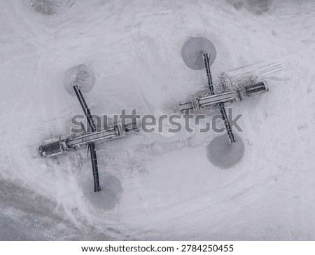 Top-down view of two mobile screening machines operating in an open-pit gypsum quarry, surrounded by white mineral dust and conveyor belt discharge piles