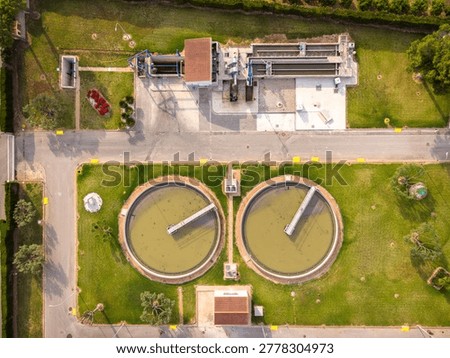 Top-down view of two secondary circular clarifiers at a wastewater treatment plant in Spain, surrounded by green lawns and industrial processing buildings