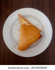 Top-down view of two triangular slices of golden-brown toasted bread, served on a white ceramic plate over dark wooden table.