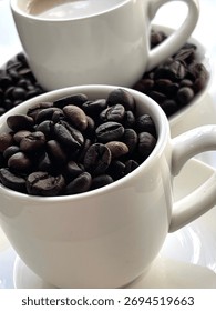 Top-down view of two white coffee cups: one filled with coffee and milk, and the other with whole roasted coffee beans, set on white saucers.