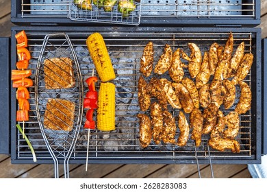 Top-down view of various foods being grilled, including seasoned chicken, corn on the cob, red bell pepper, tofu, and skewered vegetables.