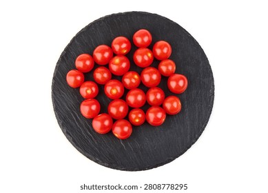 A top-down view of vibrant red cherry tomatoes neatly arranged on a round black slate serving board, isolated on a white background.