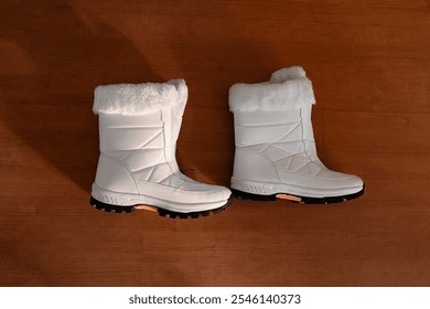 Top-down view of white winter boots with fur lining, placed on a wooden floor - Powered by Shutterstock