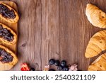 A top-down view of a wooden cutting board featuring toast with blueberry jam and croissants, elegantly arranged on a dark wooden table