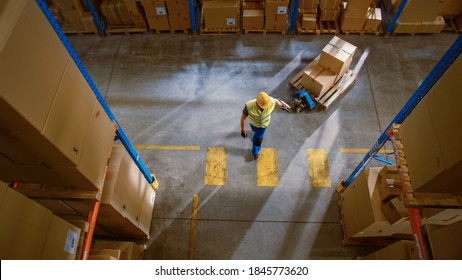 Top-Down View: Worker Moves Cardboard Boxes Using Manual Pallet Truck, Walking Between Rows Of Shelves With Goods In Retail Warehouse. People Work In Product Distribution Logistics Center