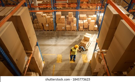 Top-Down View: Worker Moves Cardboard Boxes using Manual Pallet Truck, Walking between Rows of Shelves with Goods in Retail Warehouse. People Work in Product Distribution Logistics Center