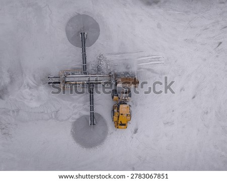 Top-down view of a yellow wheel loader dumping raw gypsum into a mobile screening plant at an open-pit quarry, surrounded by white mineral dust and tire tracks