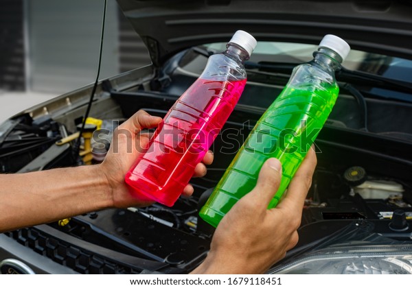 Topic of car repair shop: hands holding\
two products showing choice of pink or green coolant or antifreeze\
for cars. maintenance fluids or engine\
products.