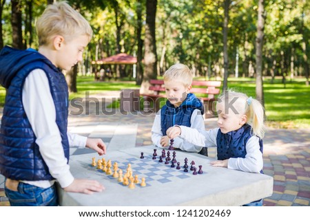 The topic children learning, logical development, mind and math, miscalculation moves advance. large family brothers and sister Caucasian boys and girl playing chess park bright sunny weather autumn.