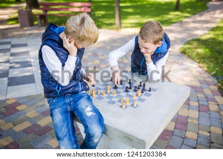 The topic is children learning, logical development, mind math, miscalculation moves advance. Big family two brothers Caucasian boys playing chess in the park in bright sunny weather in the autumn.