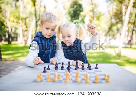 The topic children learning, logical development, mind and math, miscalculation moves advance. large family brothers and sister Caucasian boys and girl playing chess park bright sunny weather autumn.