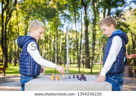 The topic is children learning, logical development, mind math, miscalculation moves advance. Big family two brothers Caucasian boys playing chess in the park in bright sunny weather in the autumn.