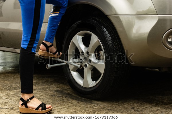 Topic of\
problems with the car on the road. Woman using force to loosen\
bolts of car tire. roadside assistance\
concept