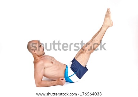 Topless man lying down on the ground doing lower abs exercise by lifting his legs up. Young guy working out on the floor. Isolated on white background.